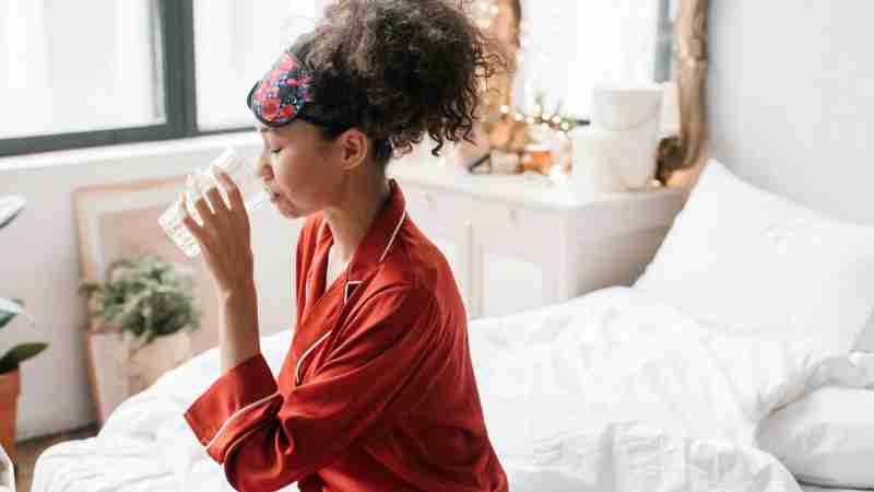 Woman in red pajamas drinking water, enhancing morning wellness rituals., tags: einfache die tag und - pexel