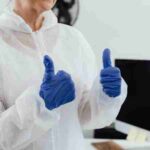 Healthcare worker in a protective suit and gloves giving a thumbs up in a laboratory setting., tags: und - pexel