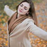 A woman with eyes closed embraces the autumn season amidst fallen leaves., tags: ruhe - pexel