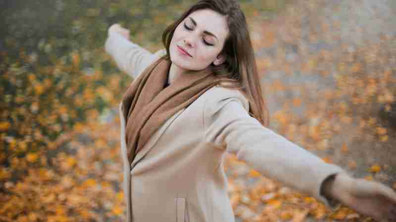 A woman with eyes closed embraces the autumn season amidst fallen leaves., tags: ruhe - pexel